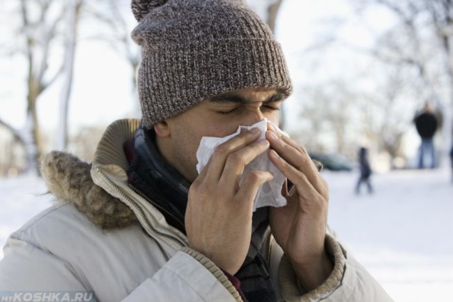 Заболевший мужчина на холоде чихает в белый платок